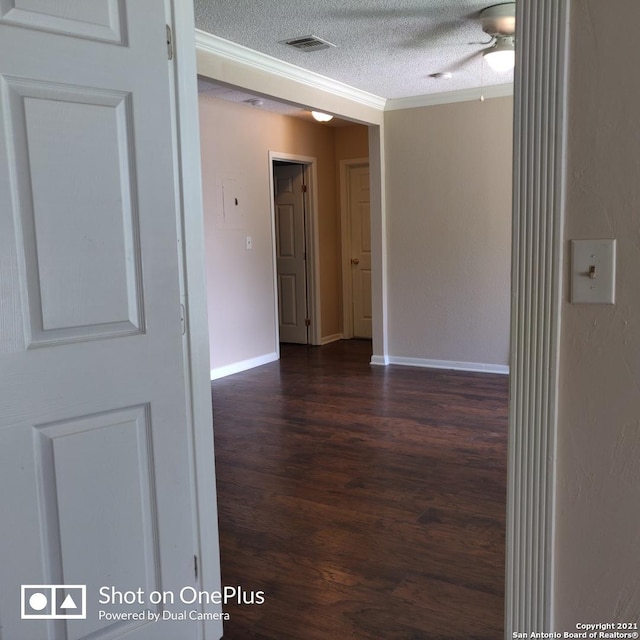 hallway featuring visible vents, baseboards, ornamental molding, a textured ceiling, and dark wood-type flooring