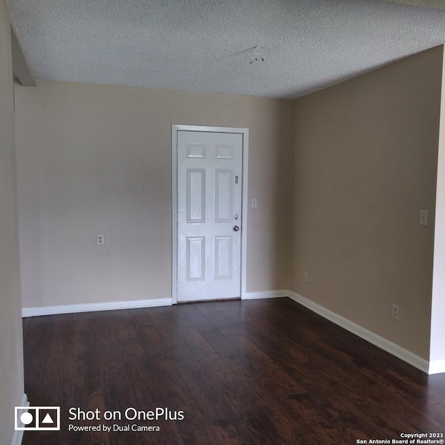 spare room with a textured ceiling, dark wood-style flooring, and baseboards