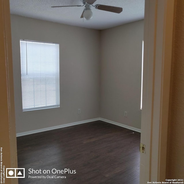 empty room with a ceiling fan, a textured ceiling, baseboards, and dark wood finished floors