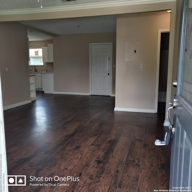 unfurnished living room with visible vents, baseboards, electric panel, dark wood-style flooring, and a sink