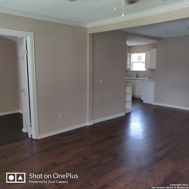 unfurnished living room featuring dark wood-style flooring, baseboards, ornamental molding, and a textured ceiling