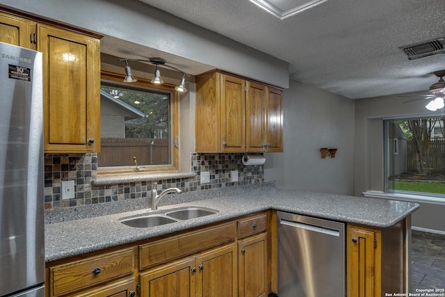 kitchen featuring appliances with stainless steel finishes, a sink, brown cabinetry, backsplash, and a peninsula