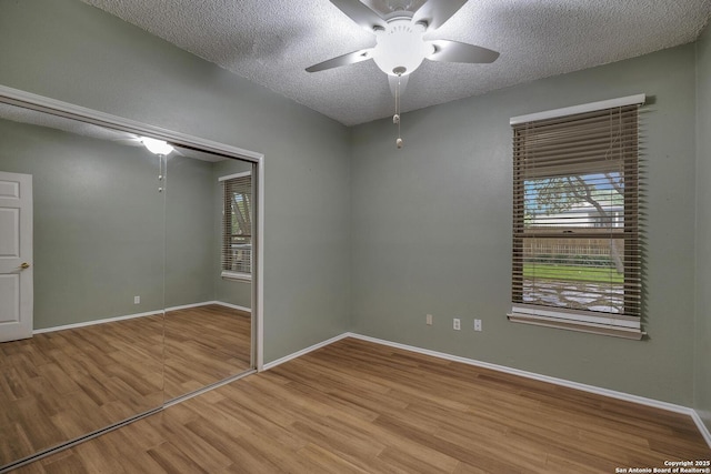 empty room with a ceiling fan, light wood-style floors, a textured ceiling, and baseboards