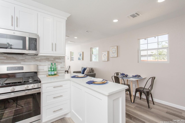 kitchen featuring visible vents, light countertops, a peninsula, stainless steel appliances, and backsplash