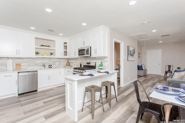 kitchen featuring visible vents, open shelves, a sink, appliances with stainless steel finishes, and a kitchen breakfast bar