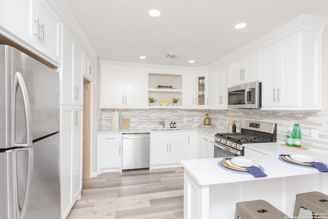 kitchen with open shelves, a sink, light countertops, appliances with stainless steel finishes, and a peninsula
