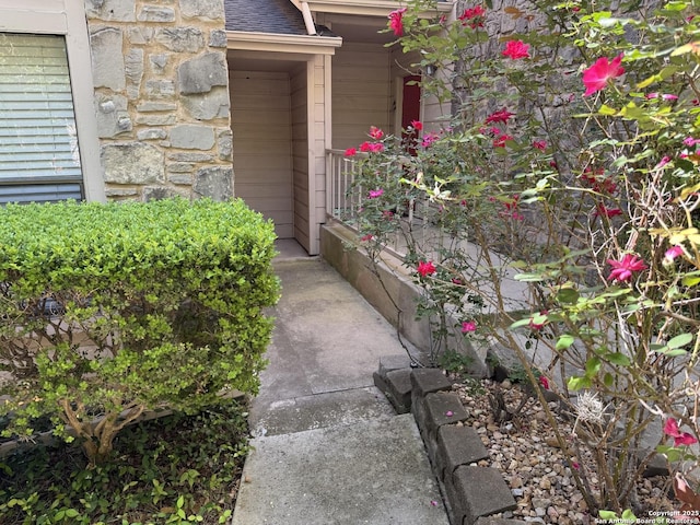 doorway to property with roof with shingles and stone siding