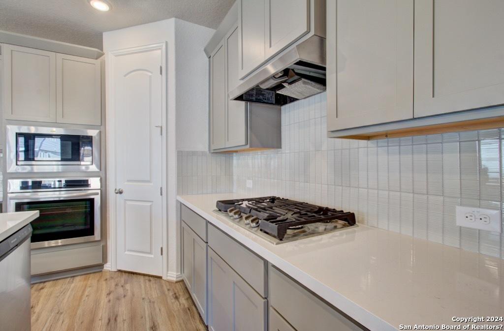2088 Adeline Way, New Braunfels, TX 78130 - kitchen with light countertops, backsplash, gray cabinetry, under cabinet range hood, and appliances with stainless steel finishes