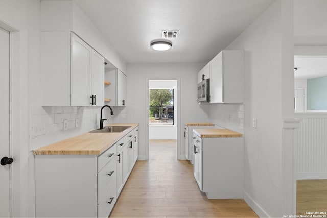 kitchen with stainless steel microwave, tasteful backsplash, open shelves, light wood-style floors, and a sink