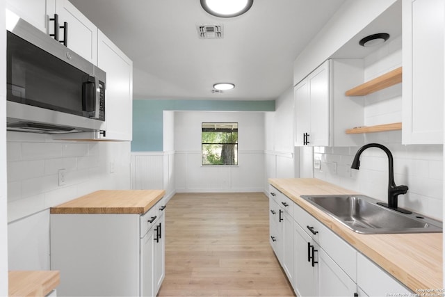 kitchen with stainless steel microwave, light wood-style flooring, open shelves, wooden counters, and a sink