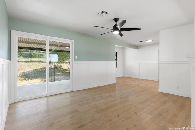 unfurnished room featuring visible vents, a ceiling fan, a wainscoted wall, and light wood-style flooring