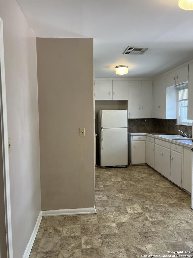 kitchen with tasteful backsplash, visible vents, baseboards, a sink, and freestanding refrigerator