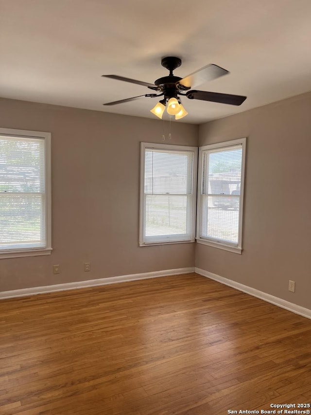 unfurnished room with baseboards, a ceiling fan, a wealth of natural light, and wood finished floors