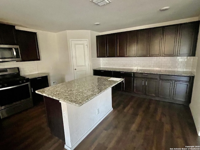 8131 Falcon Mdw, Converse, TX 78109 - kitchen featuring light stone countertops, gas stove, stainless steel microwave, dark wood-style flooring, and decorative backsplash