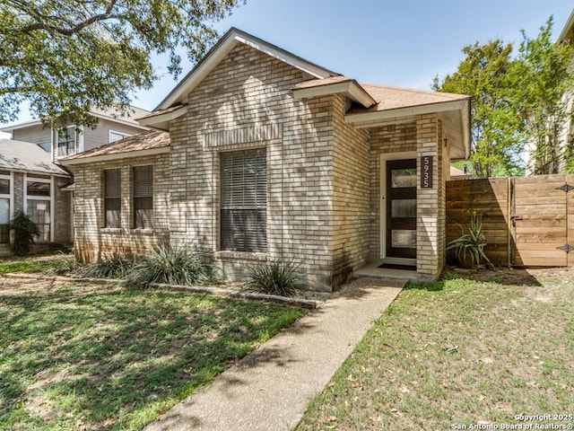 view of front of home featuring a front yard, fence, brick siding, and roof with shingles
