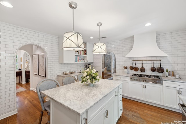 643 Terrell Rd, Terrell Hills, TX 78209 - kitchen with arched walkways, custom exhaust hood, stainless steel gas stovetop, white cabinets, and a kitchen bar