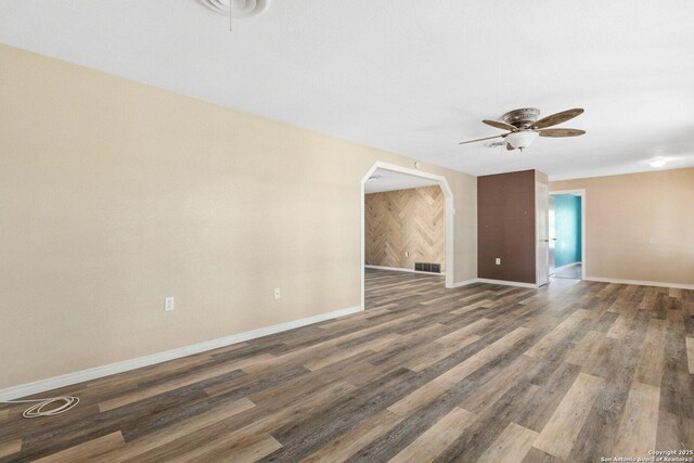 unfurnished living room featuring arched walkways, visible vents, baseboards, a ceiling fan, and wood finished floors