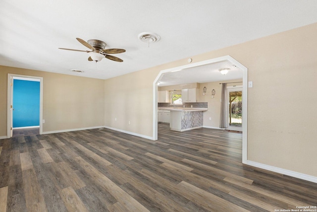 unfurnished living room with arched walkways, ceiling fan, baseboards, and dark wood-type flooring