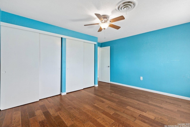 unfurnished bedroom featuring wood finished floors, visible vents, a closet, baseboards, and ceiling fan
