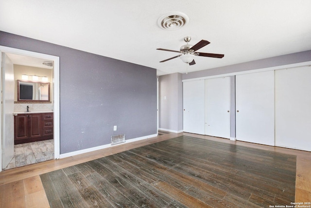 unfurnished bedroom with wood finished floors, visible vents, connected bathroom, a sink, and baseboards