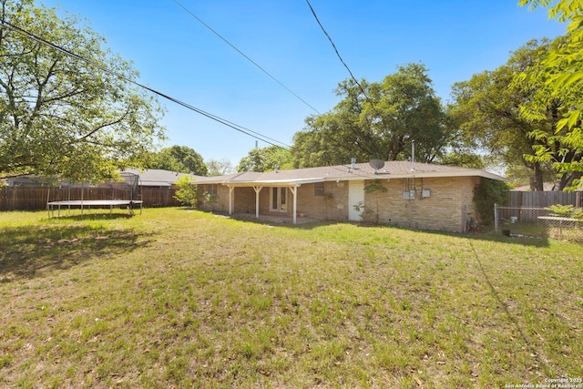 back of house featuring a fenced backyard, a yard, and a trampoline