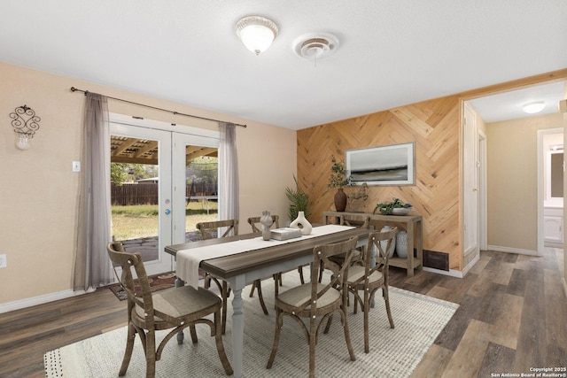 dining area with an accent wall, wooden walls, french doors, baseboards, and dark wood-type flooring