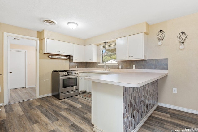 kitchen with stainless steel range with gas cooktop, a sink, light countertops, a peninsula, and dark wood-type flooring