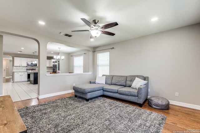 living room featuring baseboards, recessed lighting, light wood-style floors, arched walkways, and ceiling fan with notable chandelier