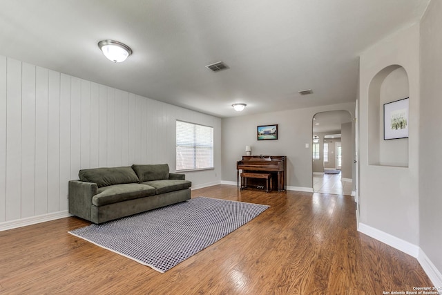 living room featuring visible vents, baseboards, arched walkways, and wood finished floors