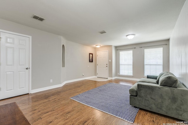 living area with arched walkways, visible vents, baseboards, and wood finished floors