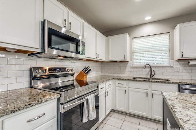 kitchen with a sink, white cabinetry, stainless steel appliances, decorative backsplash, and light tile patterned flooring