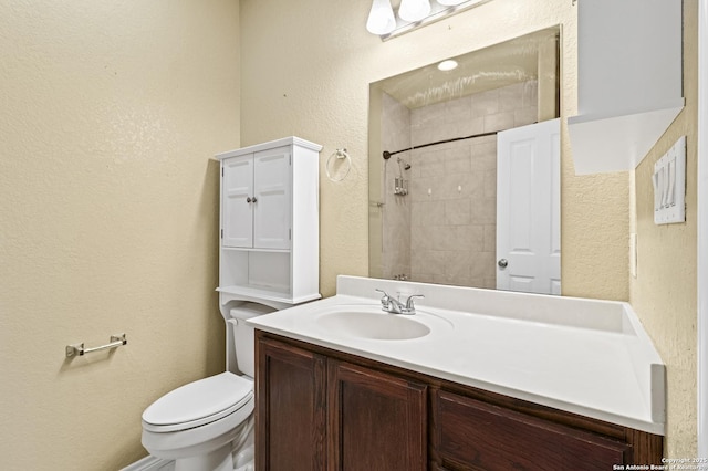 bathroom with toilet, tiled shower, a textured wall, and vanity