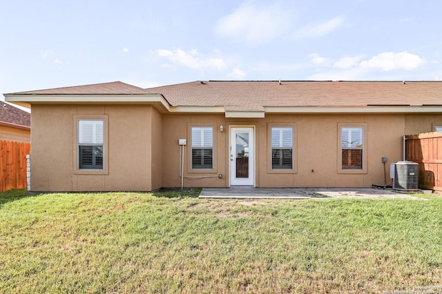 rear view of house featuring central AC unit, fence, a lawn, and stucco siding