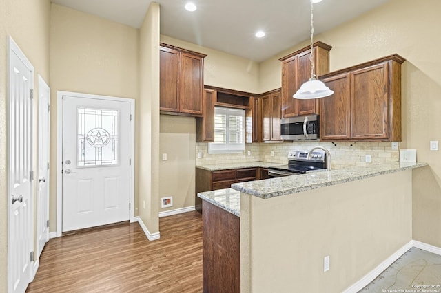 kitchen featuring a peninsula, appliances with stainless steel finishes, light wood finished floors, and backsplash