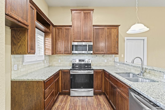 kitchen featuring dark wood-style flooring, backsplash, light stone countertops, appliances with stainless steel finishes, and a sink