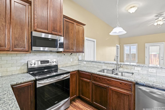 kitchen with appliances with stainless steel finishes, a ceiling fan, light stone countertops, decorative backsplash, and a sink