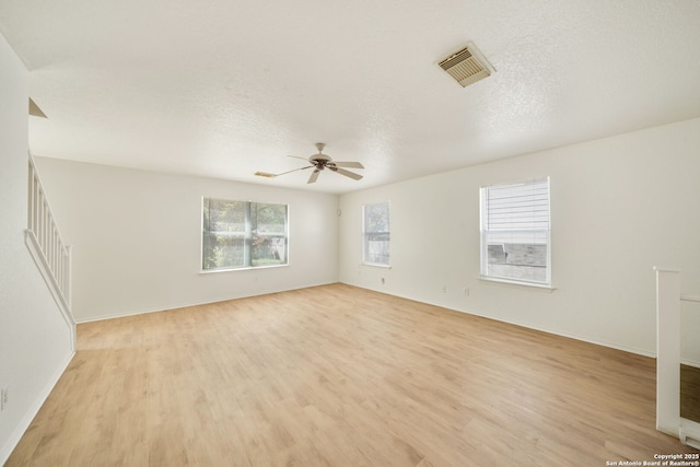 empty room featuring baseboards, light wood-type flooring, a textured ceiling, a ceiling fan, and visible vents