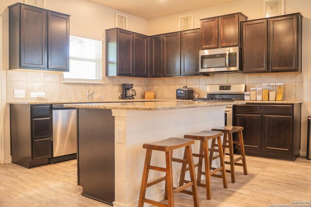 13511 Pickett, San Antonio, TX 78254 - kitchen featuring dark brown cabinetry, a breakfast bar, a kitchen island, light wood-style floors, and appliances with stainless steel finishes