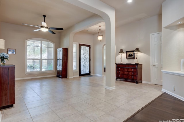 entryway featuring ceiling fan, arched walkways, light tile patterned flooring, and baseboards