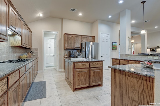 kitchen with dark stone countertops, visible vents, light tile patterned floors, freestanding refrigerator, and decorative backsplash
