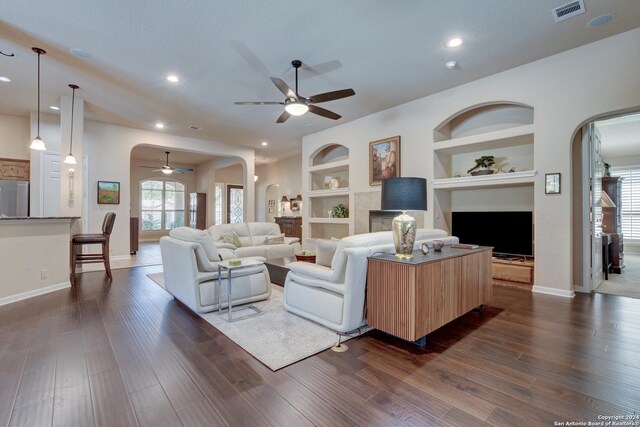 living area with built in features, ceiling fan, dark wood finished floors, arched walkways, and visible vents