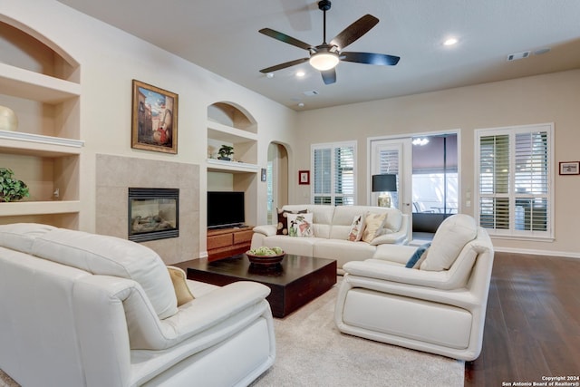 living area with built in features, baseboards, a ceiling fan, dark wood finished floors, and a tile fireplace