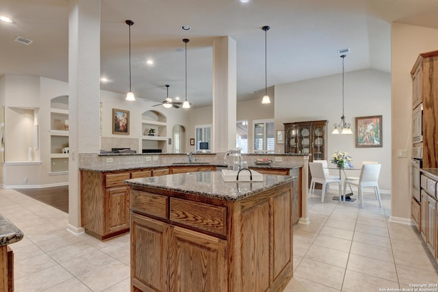 kitchen with light tile patterned floors, a sink, ceiling fan, brown cabinets, and high vaulted ceiling