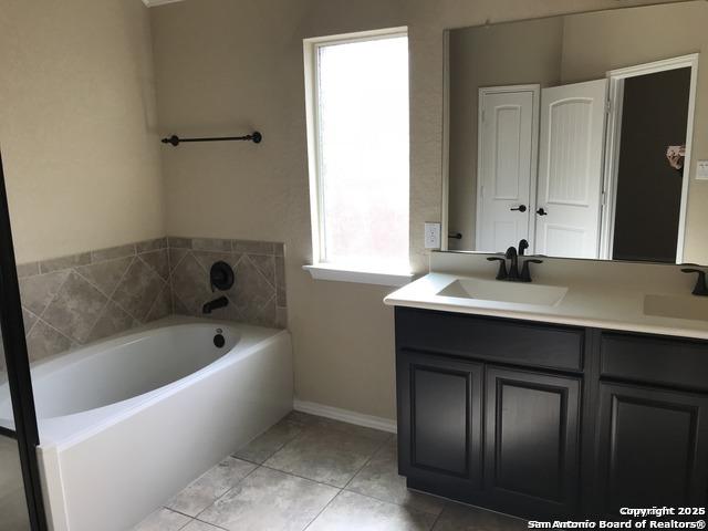 bathroom featuring a sink, baseboards, double vanity, and a garden tub