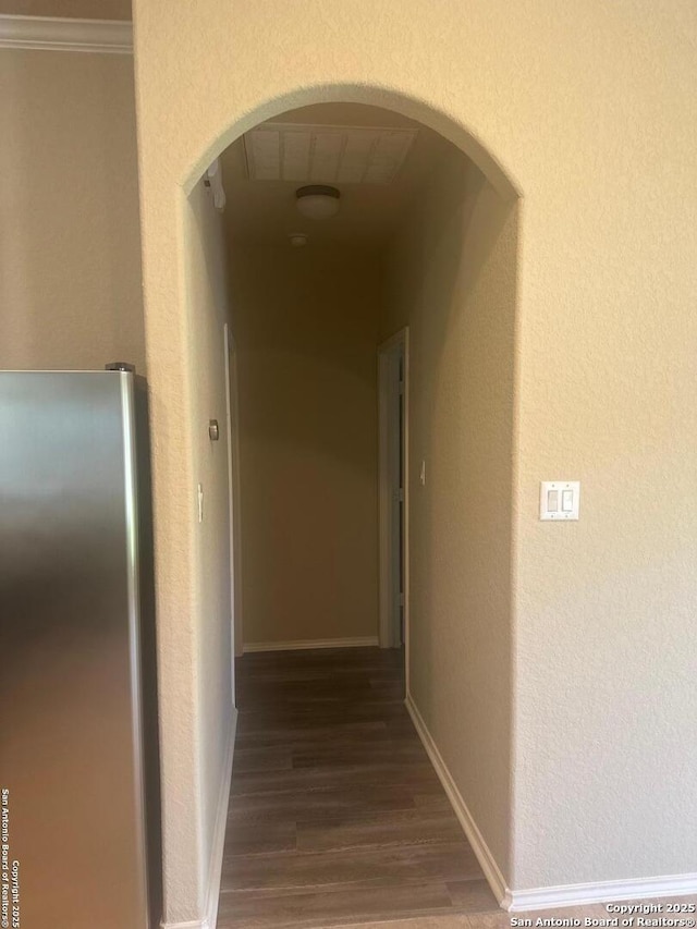 hall featuring a textured wall, arched walkways, crown molding, and wood finished floors