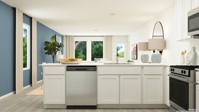 kitchen with light wood-style flooring, a peninsula, a sink, light countertops, and stainless steel appliances