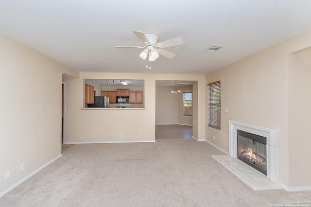 unfurnished living room with visible vents, baseboards, a warm lit fireplace, a ceiling fan, and light colored carpet