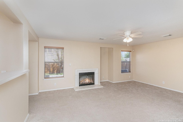 unfurnished living room with visible vents, baseboards, a ceiling fan, a lit fireplace, and carpet flooring