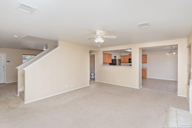 unfurnished living room with ceiling fan with notable chandelier, light colored carpet, baseboards, and visible vents