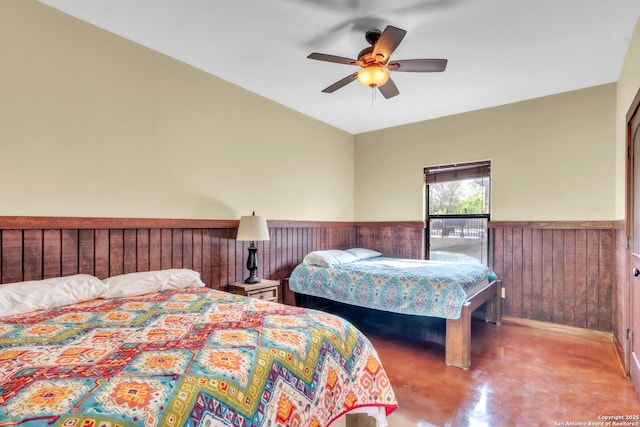 723 Tierra Linda, Concan, TX 78838 - bedroom with concrete floors, wood walls, ceiling fan, and wainscoting